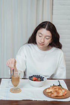 Woman having breakfast with coffee, berries, and croissant indoors.
