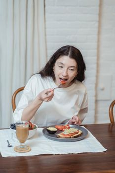 A woman eating a nutritious breakfast with coffee and fruit at home.