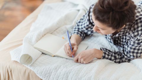 A woman writes in a journal while relaxing on a cozy bed with soft lighting and peaceful surroundings.