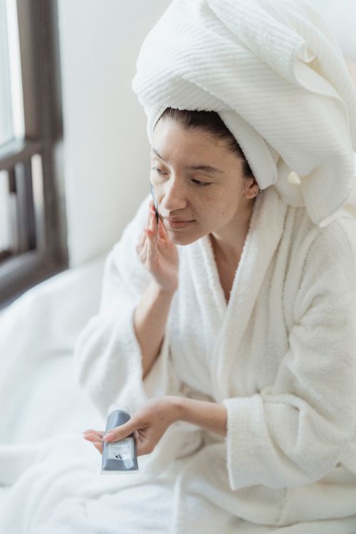 Free Woman in a bathrobe applies face cream in a serene indoor setting Stock Photo