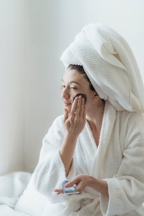 Free Woman Wearing a Robe Putting Face Cream Stock Photo