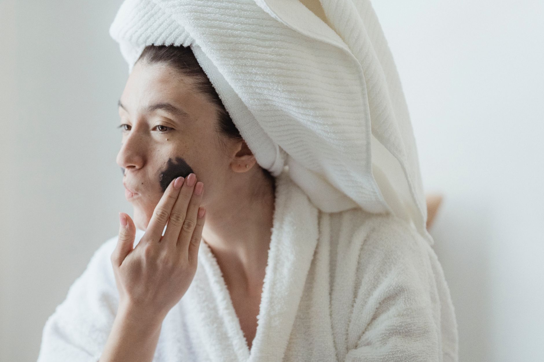 Woman applying a rejuvenating face mask in a home spa setting.