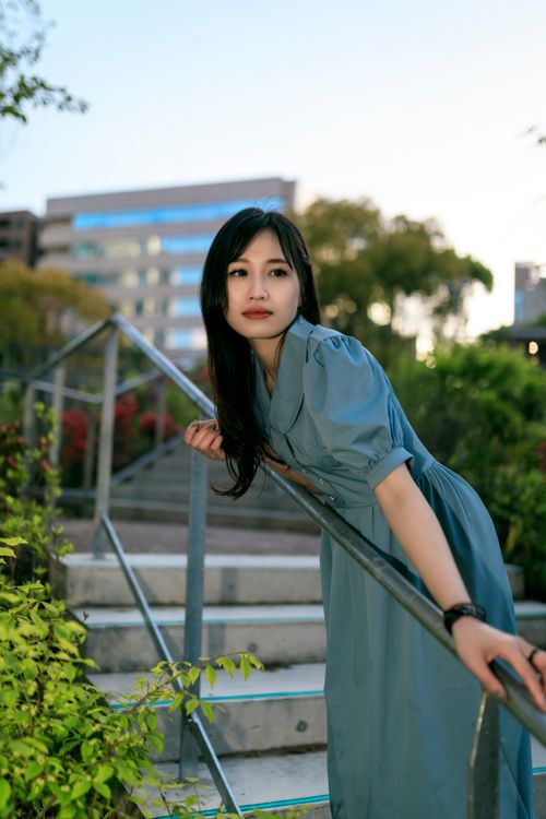 Free Elegant woman in blue dress leaning on a railing outdoors, conveying a serene mood. Stock Photo