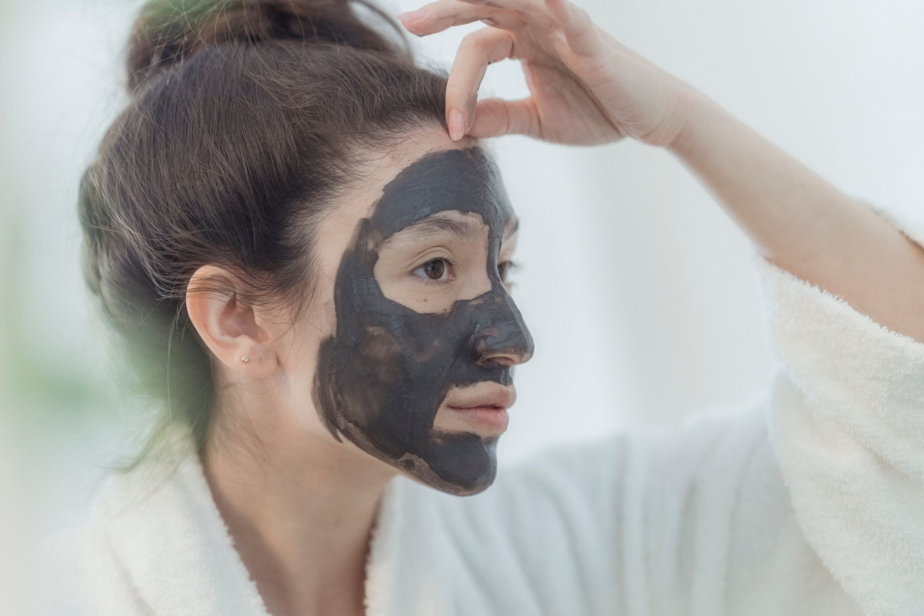Woman in robe applying a clay face mask, focusing on skincare routine and beauty treatment.