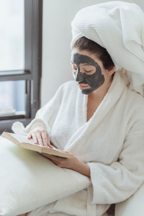 Free Woman enjoying a skincare mask while reading in a cozy indoor setting. Stock Photo