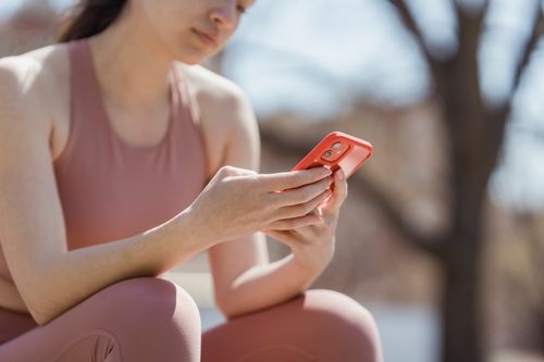 Free Woman in workout attire checking smartphone outdoors, enjoying a sunny day. Stock Photo
