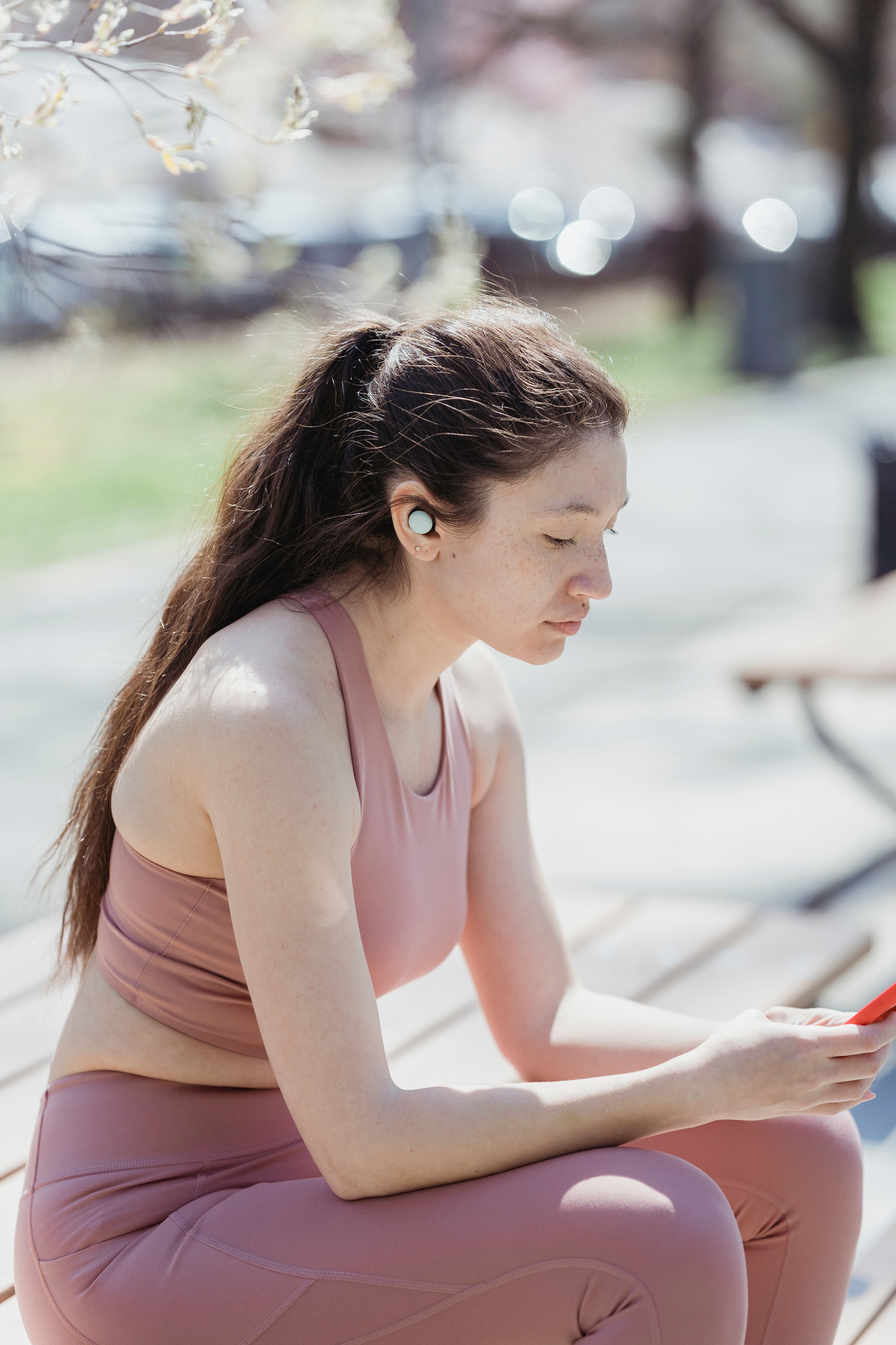 Young woman listening to music with earbuds while using smartphone on a sunny day.