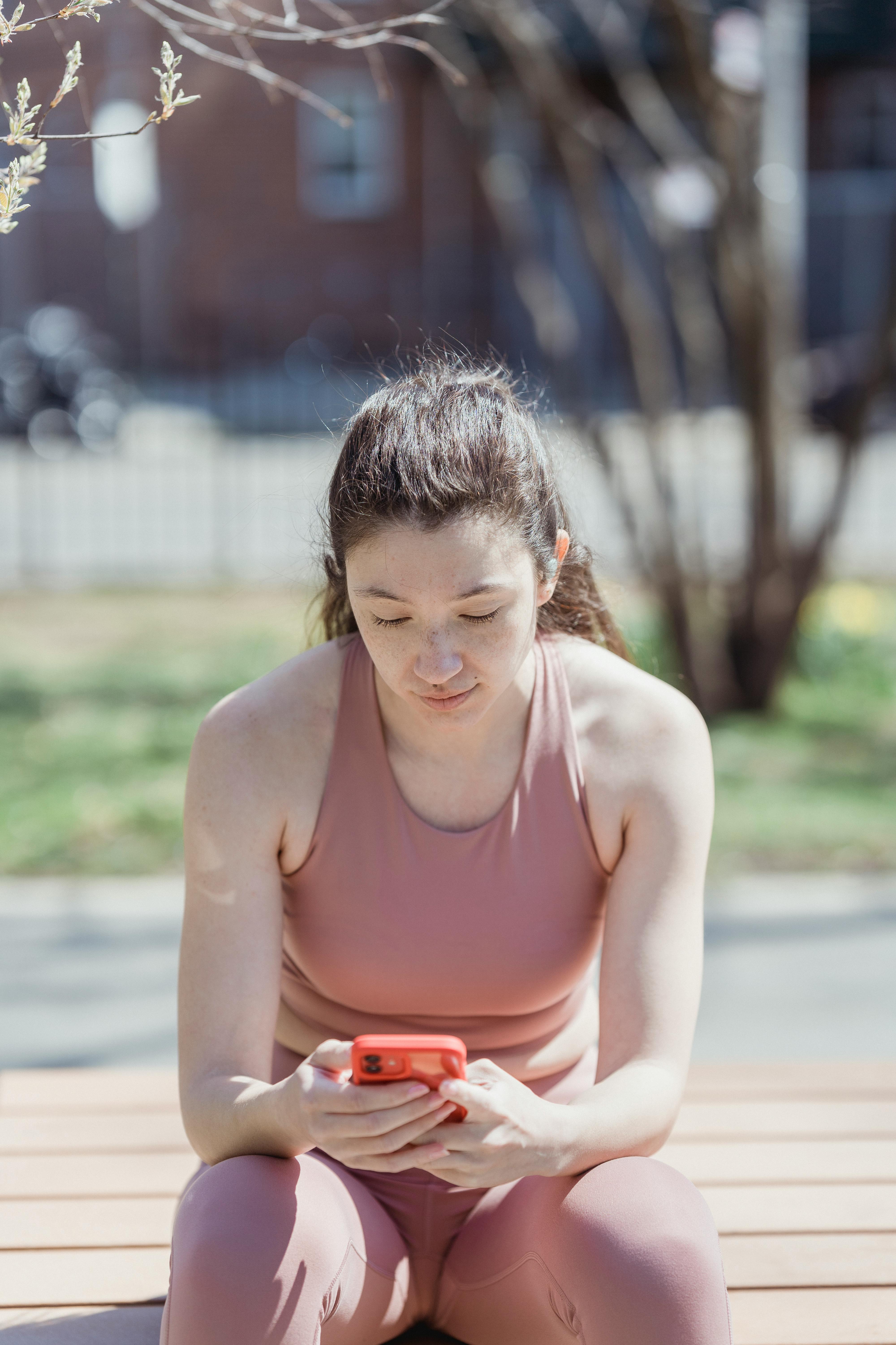 woman in sports clothing sitting outdoors and using phone