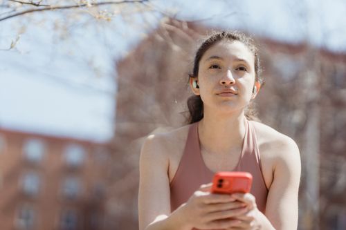 Free Young woman with earbuds using her smartphone outside on a sunny day. Stock Photo