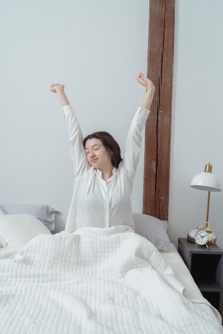 A woman waking rested and stretching in morning light, an alarm clock on the nightstand.