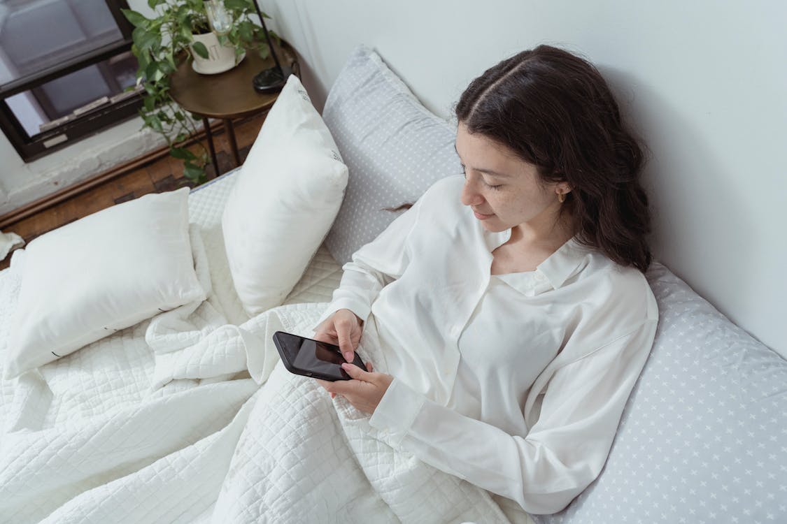 Free A Woman Looking at Her Smartphone While in Bed  Stock Photo