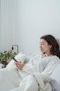 Woman Wearing White Pyjama Lying in Bed with Mobile Phone