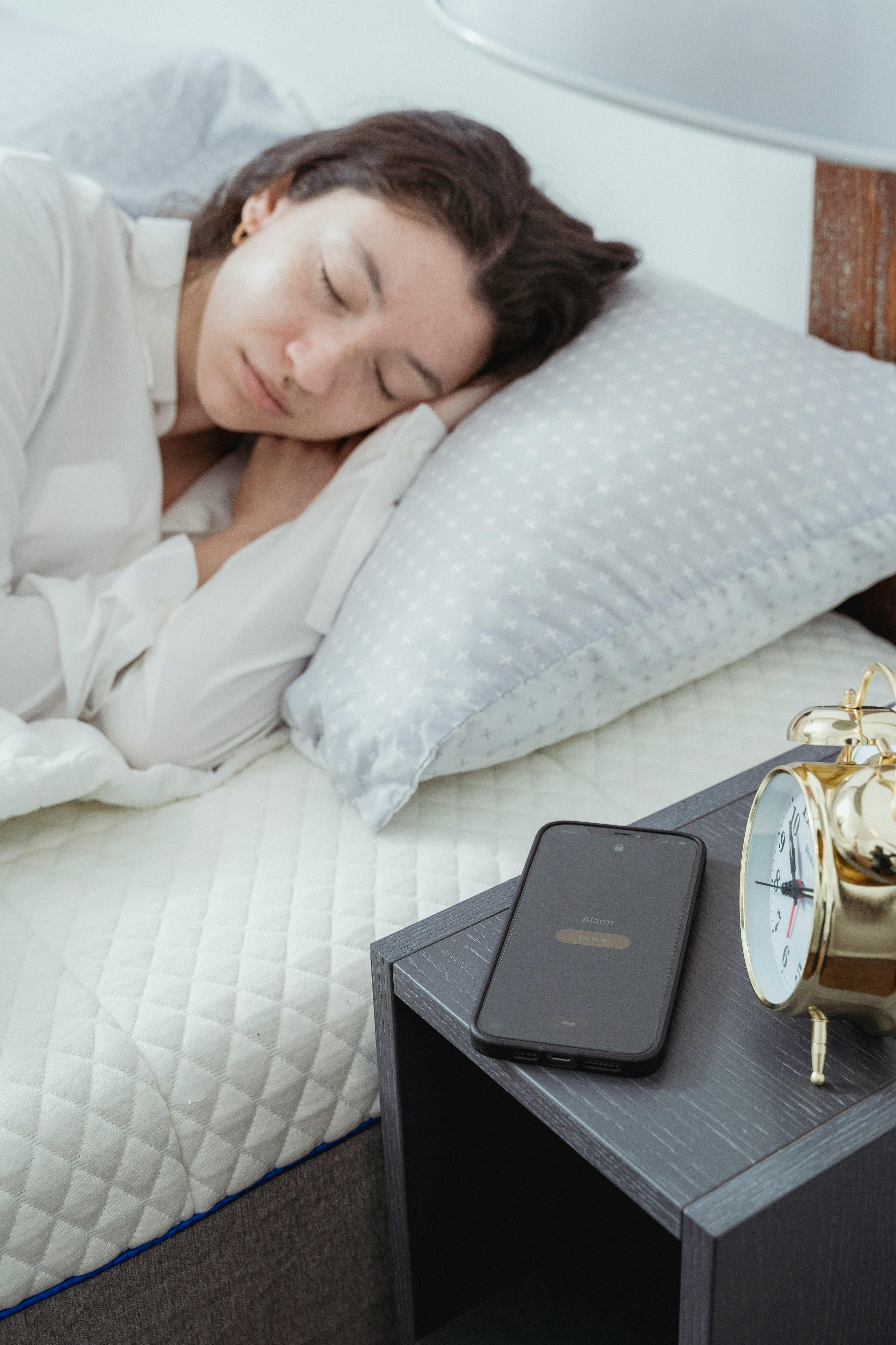 A woman sleeps peacefully in a cozy bedroom with an alarm clock and smartphone nearby.