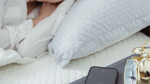 A woman sleeps peacefully in a cozy bedroom with an alarm clock and smartphone nearby.