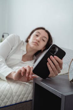 A woman lying on a bed holding a smartphone, captured in a relaxed setting.