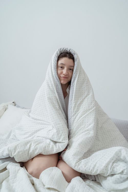 Free Young woman wrapped in a blanket sitting on the bed, creating a cozy and relaxed atmosphere indoors. Stock Photo