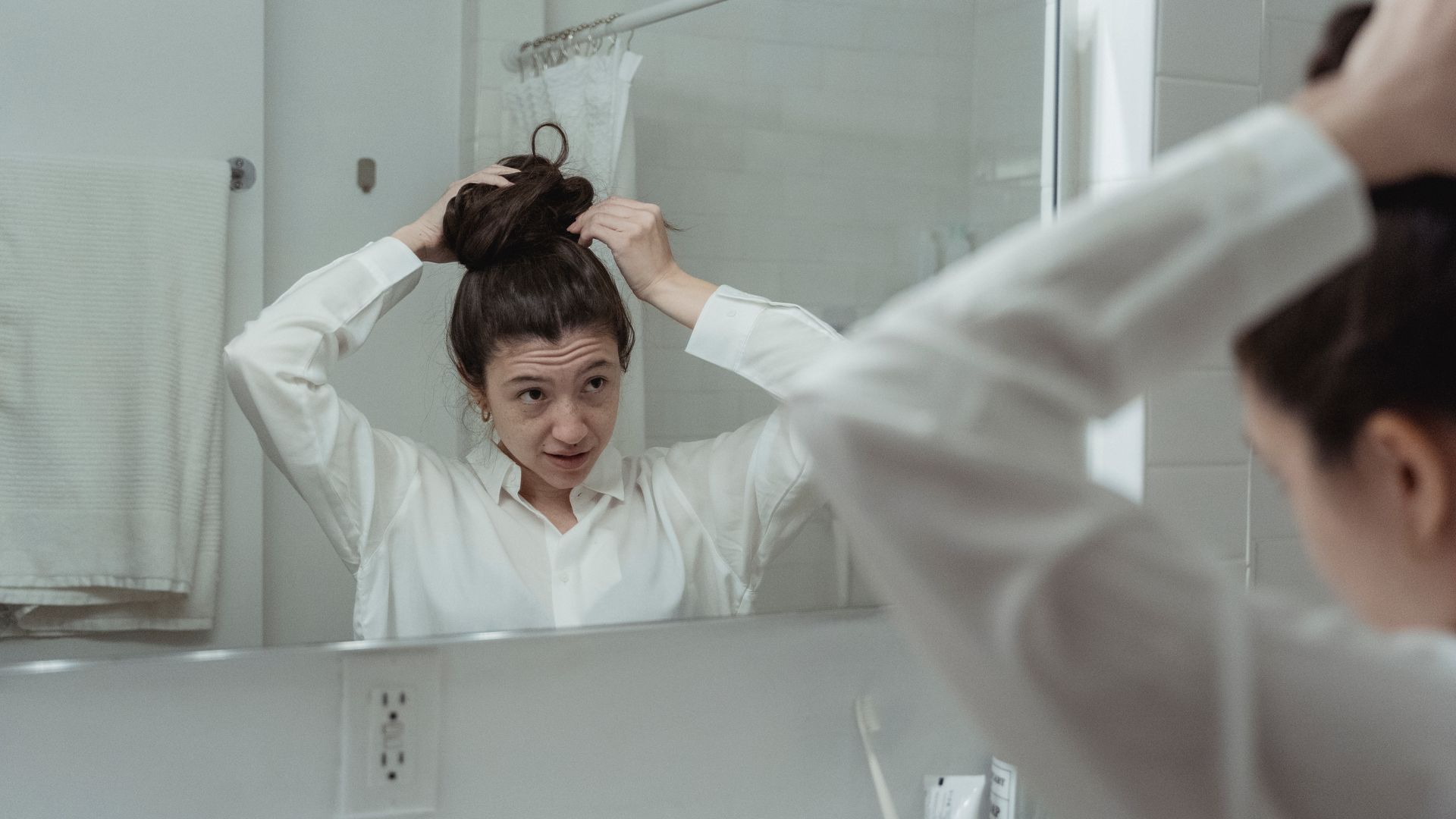 Modafinil Hair Thinning Myth: Unraveling the Truth Woman styling her hair in front of bathroom mirror wearing a white shirt — modafinil hair thinning myth