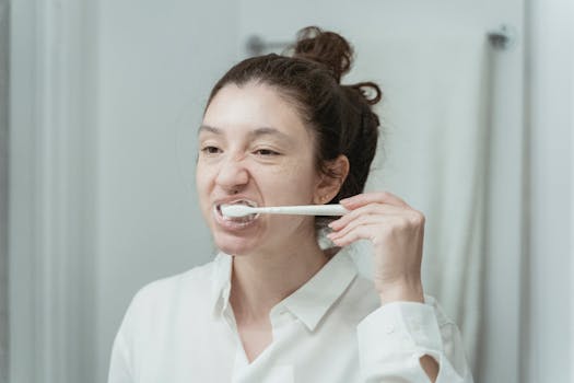 A young woman brushes her teeth in front of a bathroom mirror, focusing on oral hygiene.