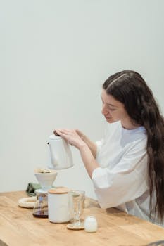 Woman making pour over coffee at a wooden table indoors, focusing on a mindful brewing process.
