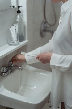 A woman in a bathroom prepares her toothbrush above a clean, white sink.
