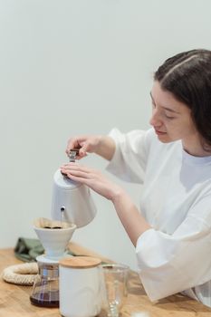 A woman in a white shirt pouring hot water into a coffee filter for a fresh brew.