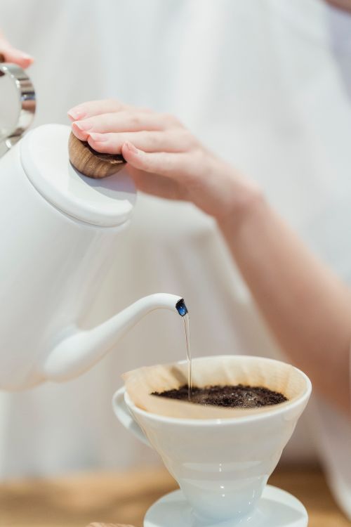 Free White porcelain kettle pouring hot water over ground coffee in a dripper. Stock Photo