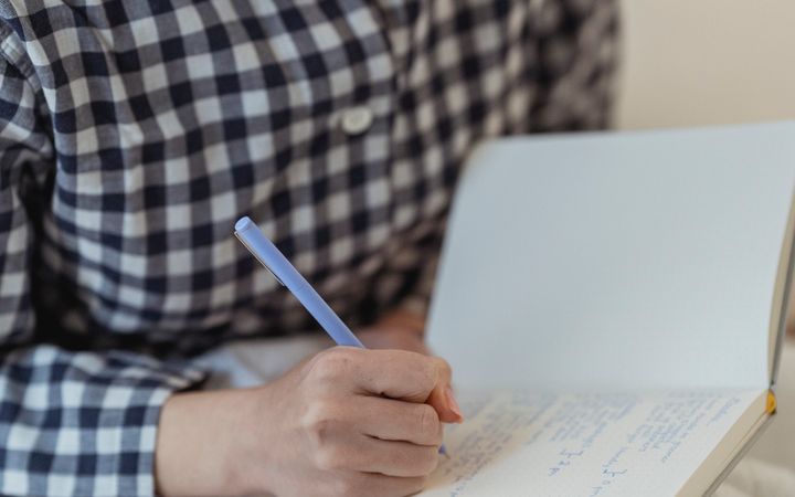 A young woman in a plaid shirt writing notes in her notebook, focusing on her thoughts.