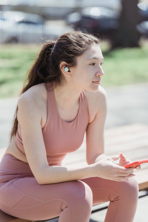 Free Woman in pink activewear sitting outdoors using smartphone. Perfect for lifestyle and fitness themes. Stock Photo