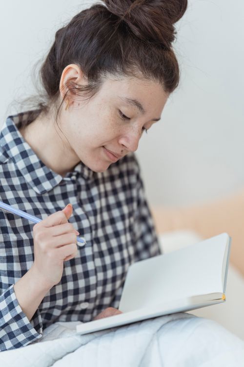 Free Young woman with pen journaling in a blank notebook, sitting indoors. Stock Photo