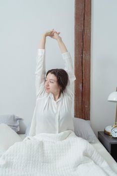 Woman stretching in bed with white bedding, creating a cozy morning atmosphere.