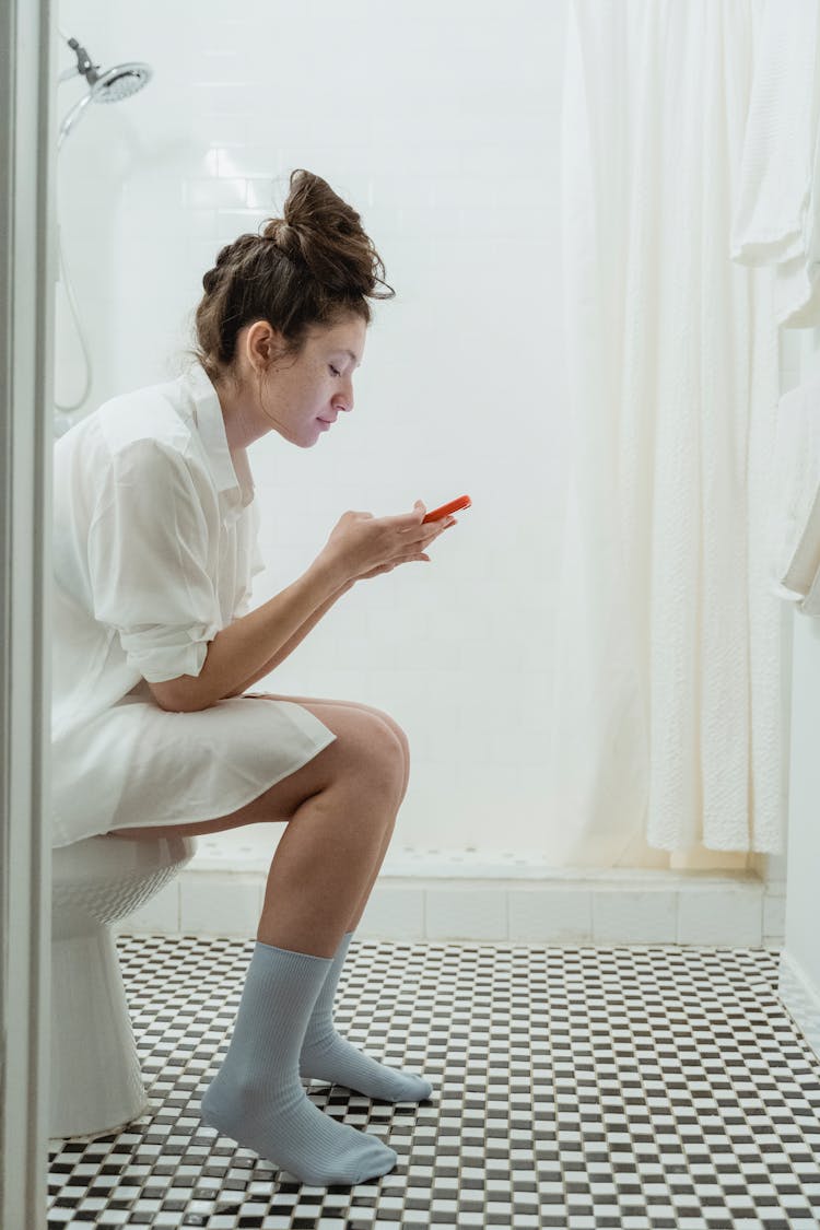 Woman Sitting On A Toilet And Using Phone 