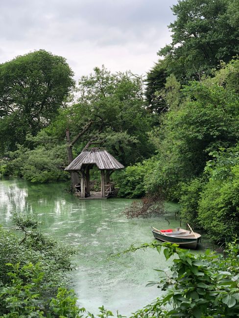 Peaceful scene of a gazebo by a lush green pond with a moored boat in New York.