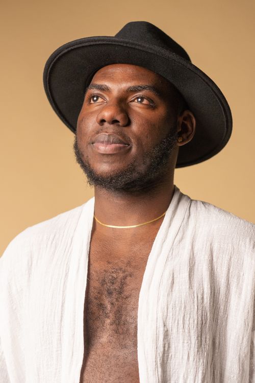 Free Close-up portrait of a man with a black hat and white attire against a soft brown background. Stock Photo