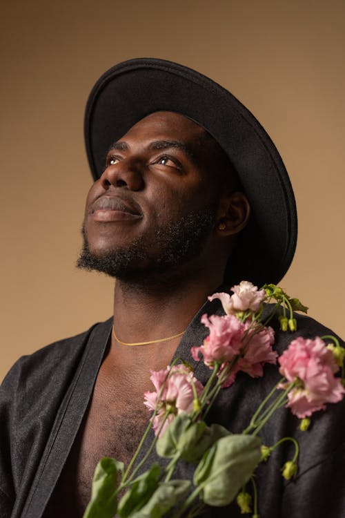Free Close-Up Shot of a Man in Black Sleeves and Black Hat Holding Pink Flowers Stock Photo