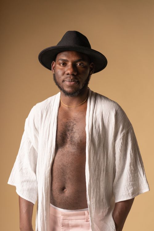 Free Elegant portrait of a man wearing a black hat and white attire against a brown backdrop. Stock Photo