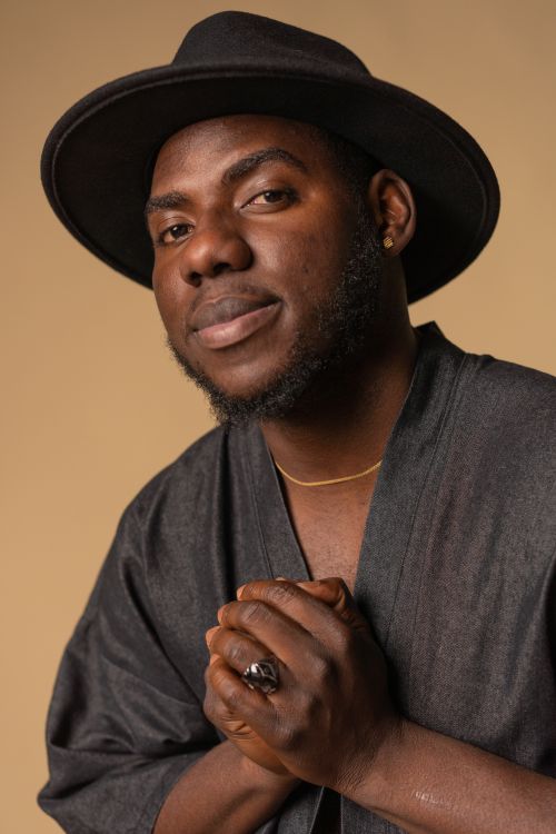 Free Close-up portrait of a man wearing a black hat and attire against a brown background. Stock Photo