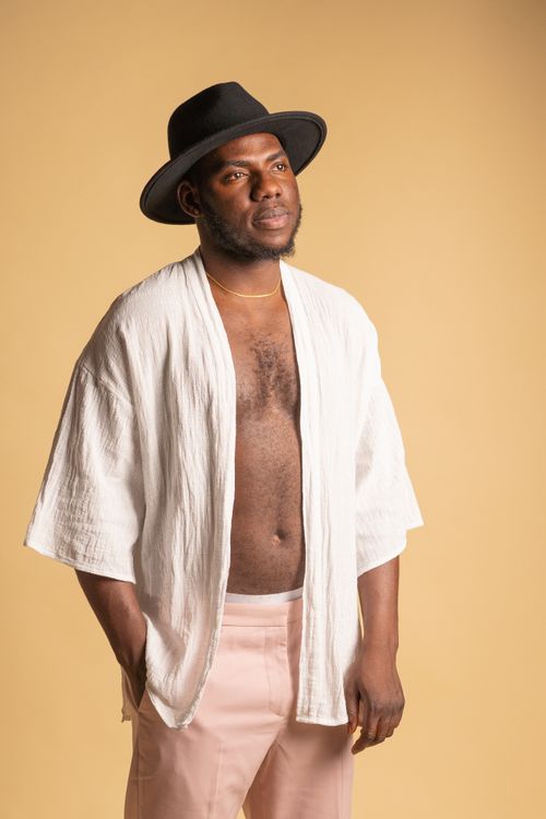 Free A confident man with a beard poses in a stylish black fedora hat and casual clothing against a neutral background. Stock Photo