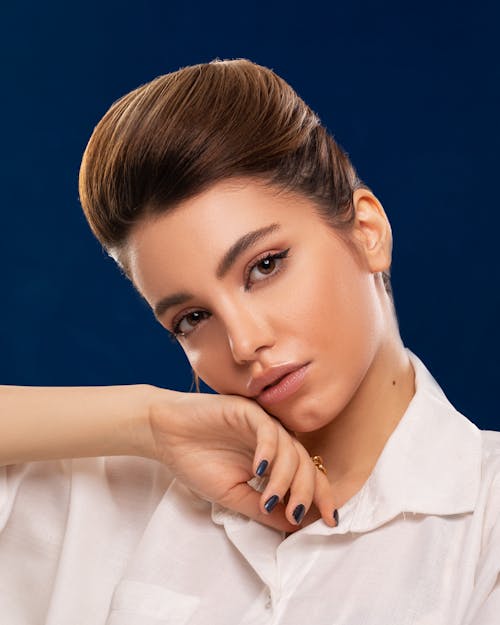 Alluring model with hairdo touching face on blue background