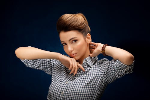 Stylish young woman with hairdo touching neck and chin while looking at camera with deep gaze