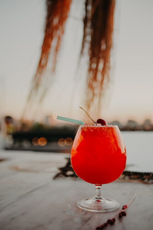 Free Glass of bright red refreshing cocktail with ice and straw decorated with cherry on wooden surface on summer evening Stock Photo
