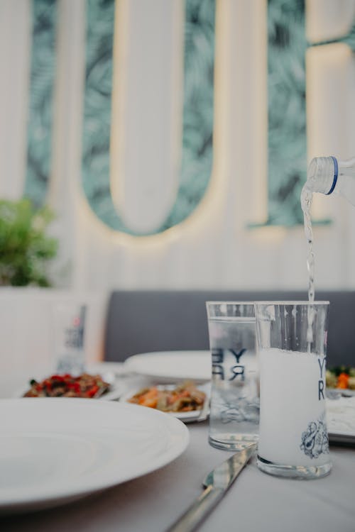 Glasses of sparkling water placed on table with delicious appetizers and tableware in light white restaurant