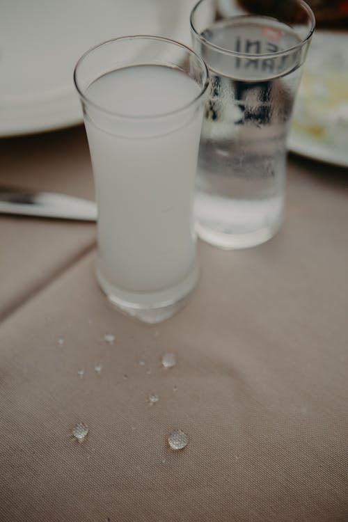 From above of crystal shots with alcoholic drinks served on table with plates and silverware in restaurant