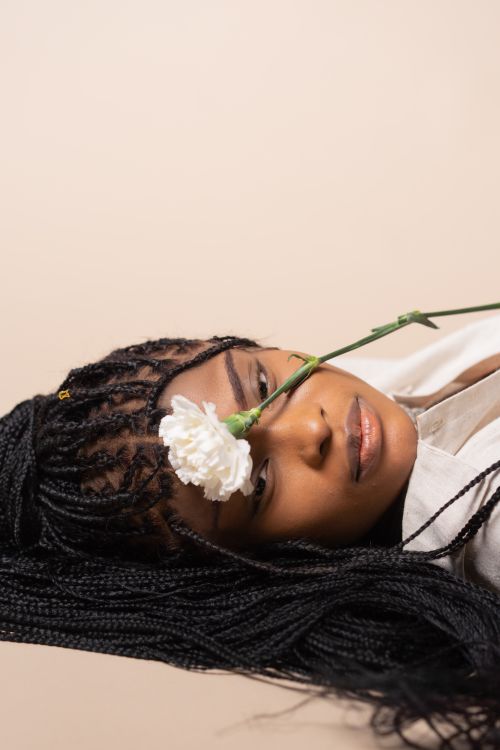 Free Studio portrait of a woman with braided hair and a white flower over her face, creating a serene atmosphere. Stock Photo