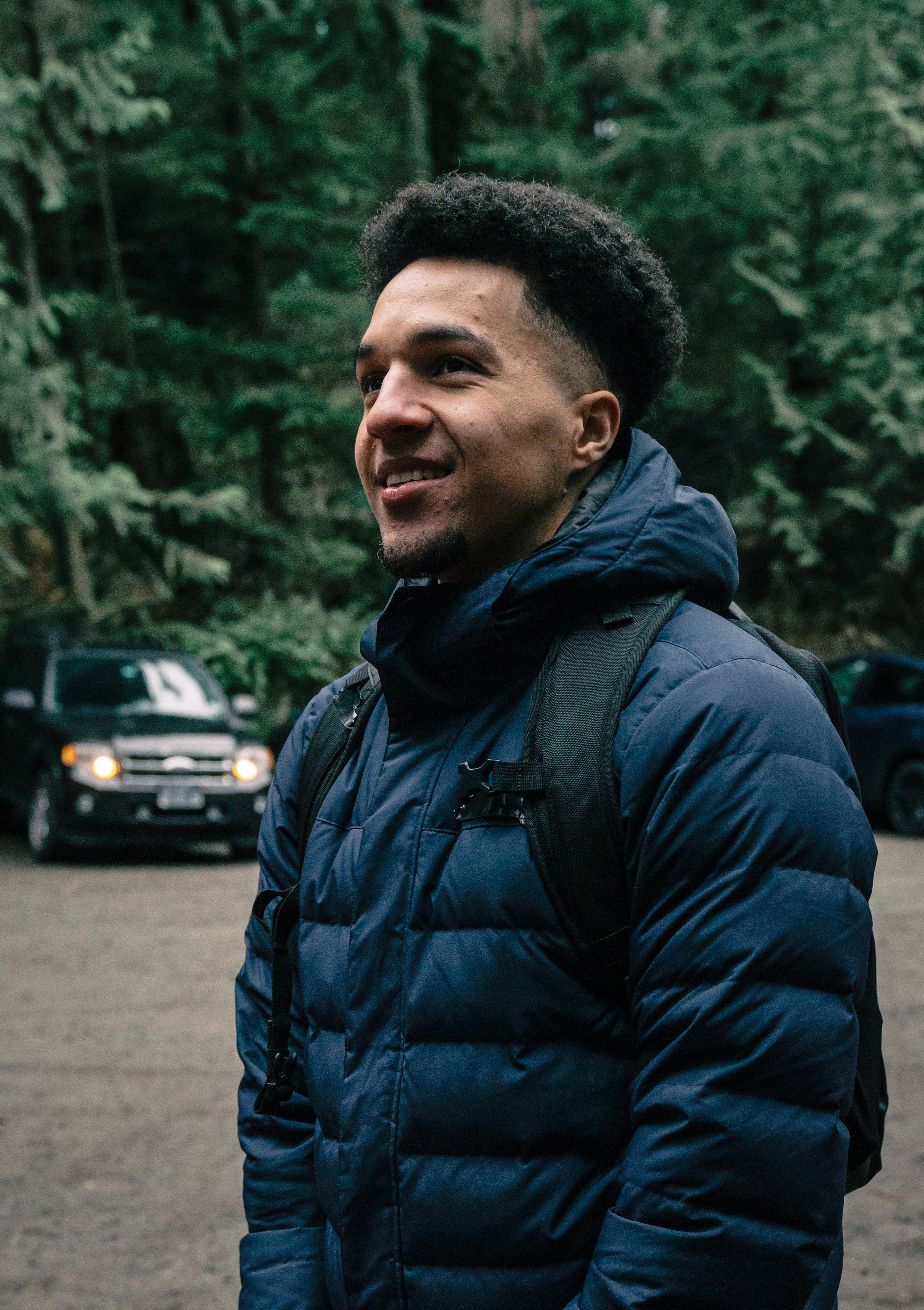 A happy man wearing hiking gear stands outdoors in a forest.
