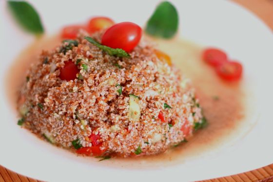 Mound of tomato-tinted bulgur salad with cherry tomatoes and mint in a white bowl