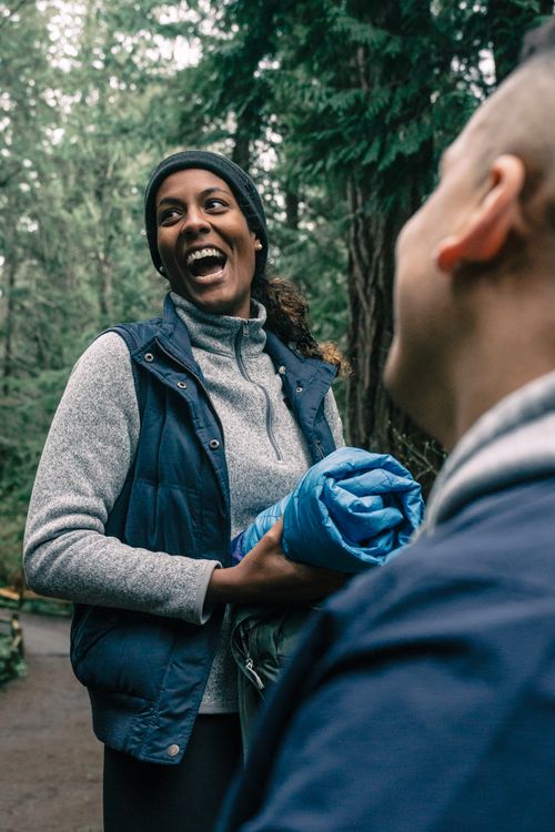 Free Two friends laughing and holding a jacket during a hike in a forest. Stock Photo
