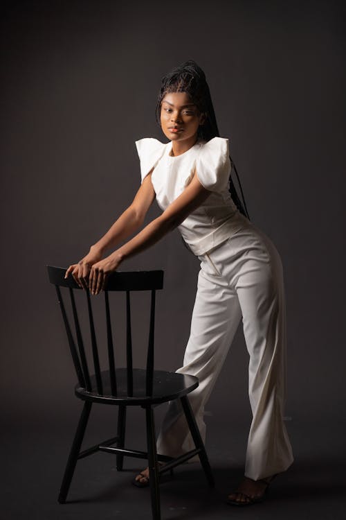 Woman in White Top and White Pants Holding on Black Chair