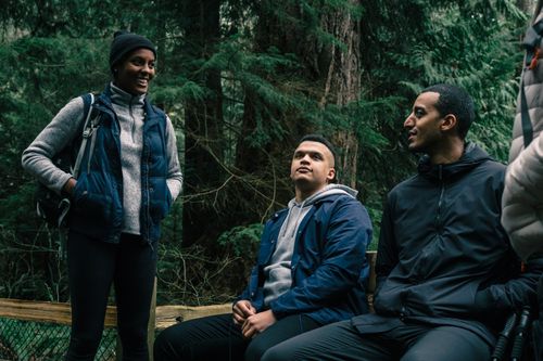 Free Three friends hiking and relaxing in a lush forest setting, engaging in conversation. Stock Photo
