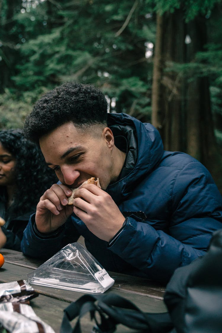 Man In Blue Bubble Jacket Eating Sandwich