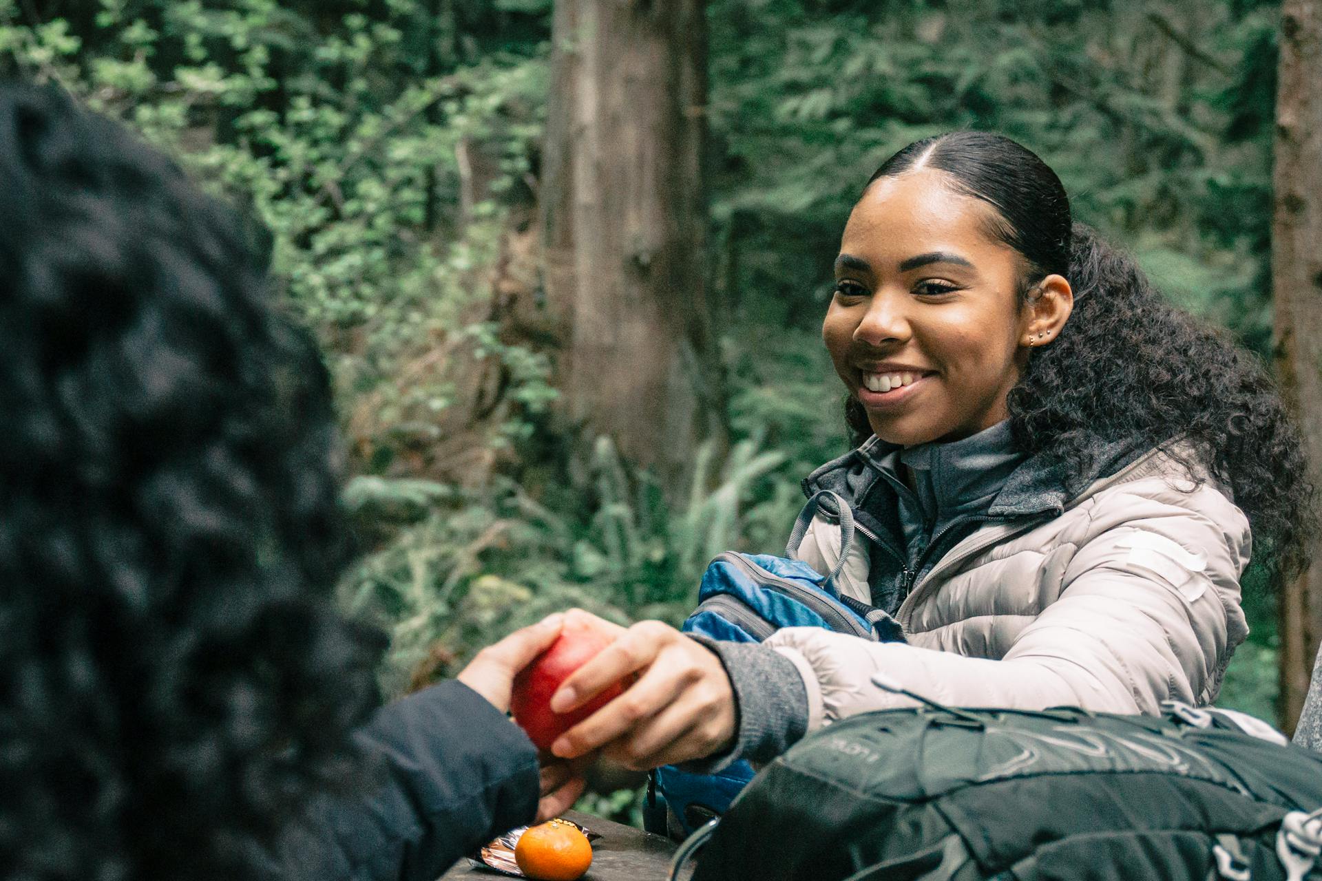 Woman in hiking gear shares an apple with a friend during a forest hike, showcasing joy and companionship.